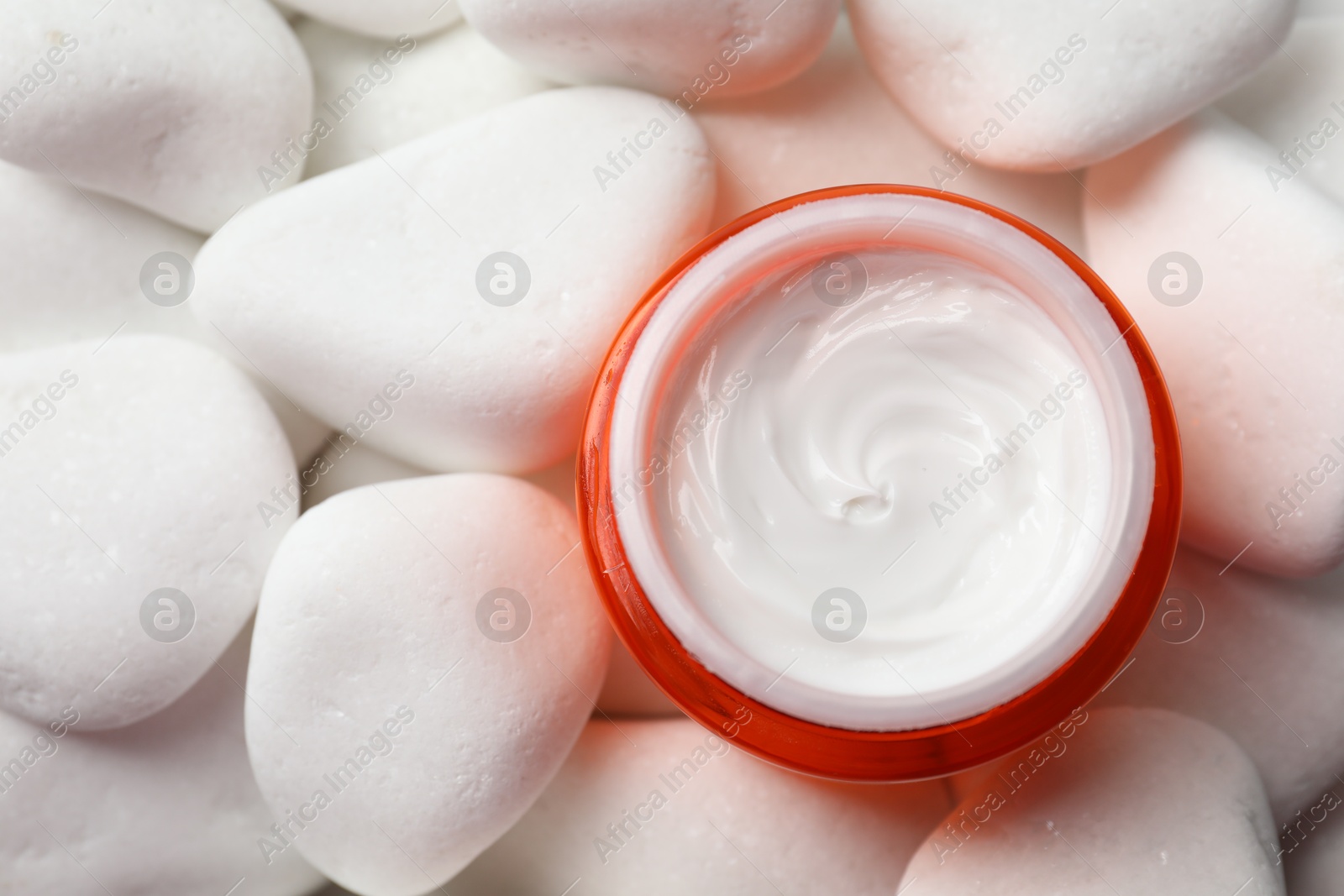 Photo of Jar of nourishing cream on white pebble stones, top view