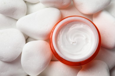 Photo of Jar of nourishing cream on white pebble stones, top view