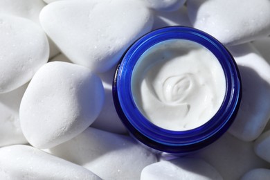 Photo of Jar of nourishing cream on white pebble stones, top view