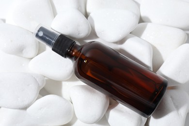 Photo of Spray bottle of cosmetic product on white pebble stones, top view