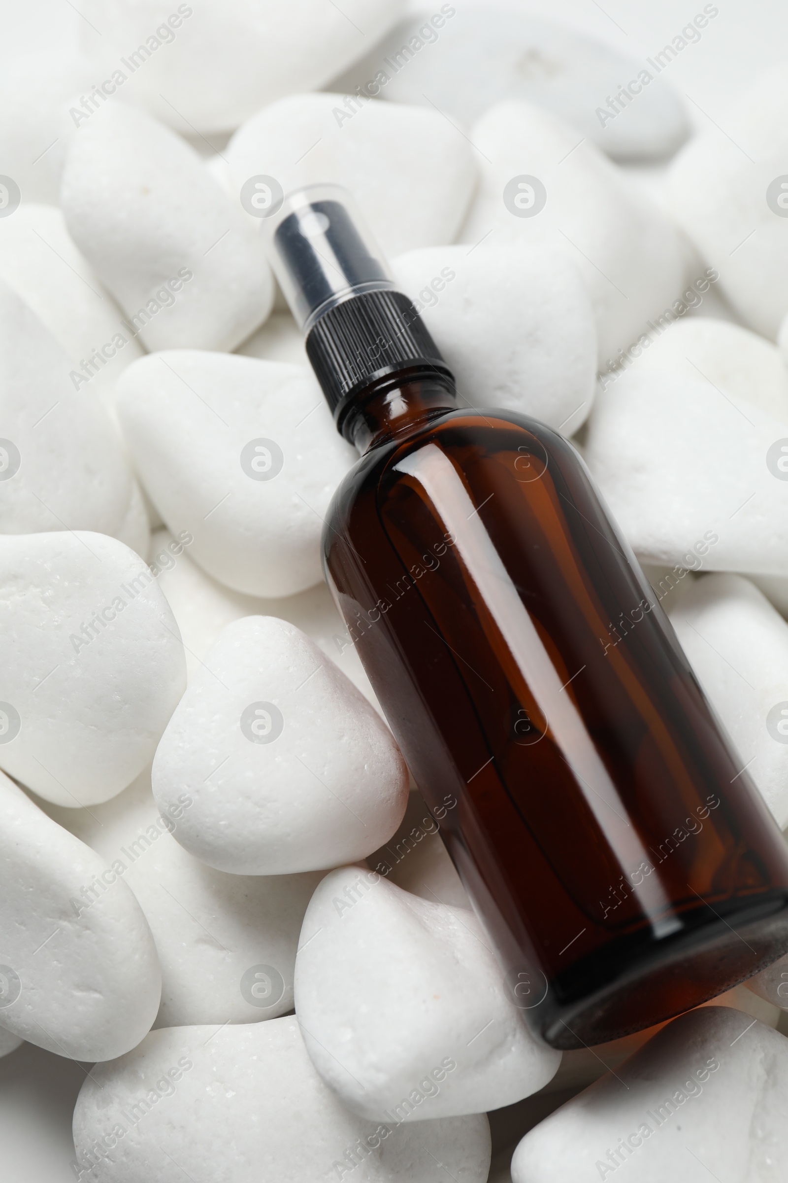 Photo of Spray bottle of cosmetic product on white pebble stones, closeup