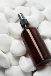 Spray bottle of cosmetic product on white pebble stones, closeup