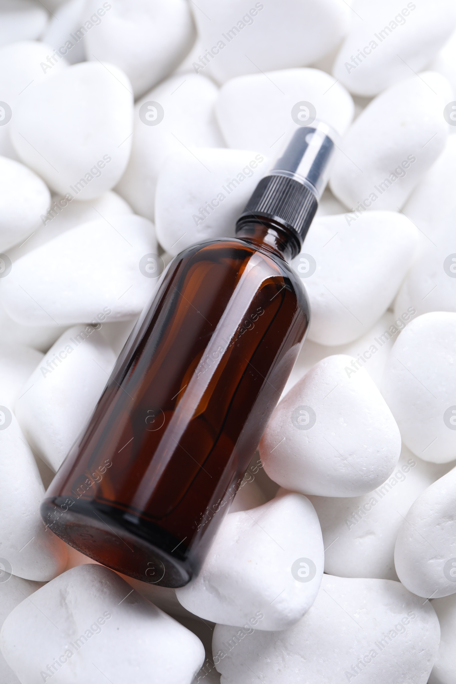 Photo of Spray bottle of cosmetic product on white pebble stones, closeup