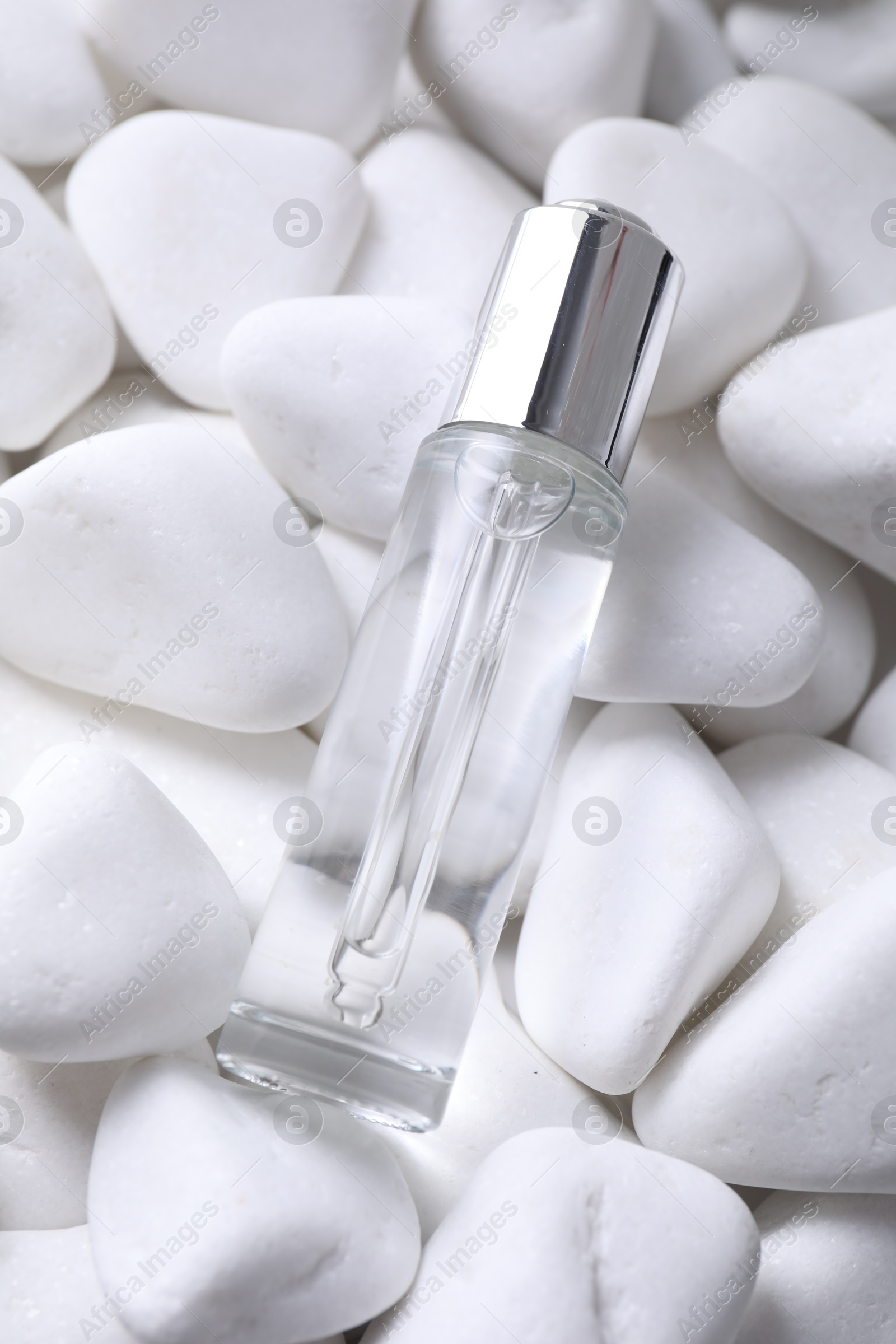 Photo of Bottle of serum on white pebble stones, above view