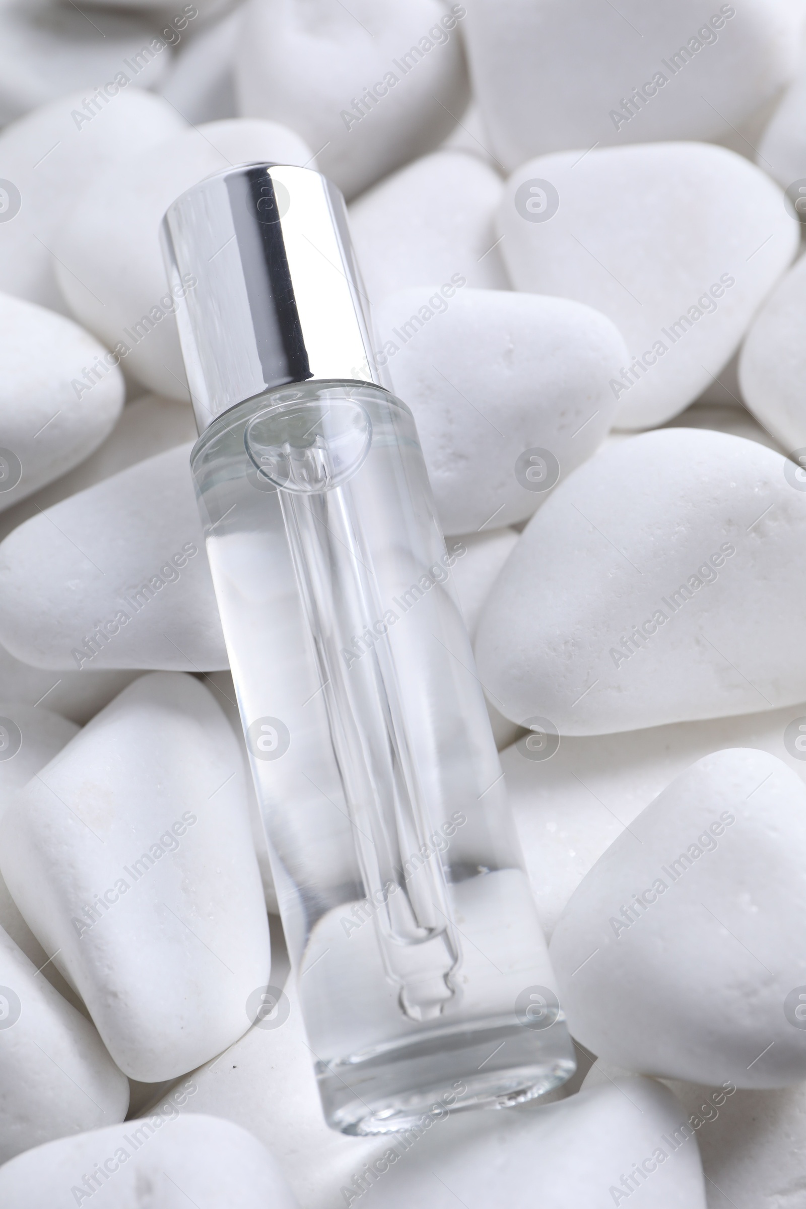 Photo of Bottle of serum on white pebble stones, closeup