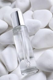 Bottle of serum on white pebble stones, closeup