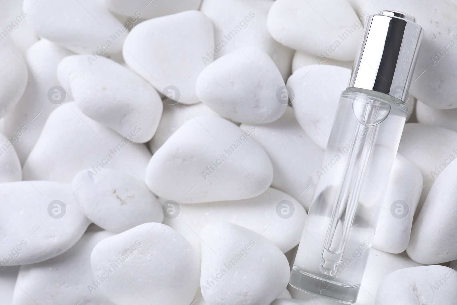 Photo of Bottle of serum on white pebble stones, top view