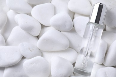 Bottle of serum on white pebble stones, top view