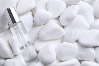 Bottle of serum on white pebble stones, top view