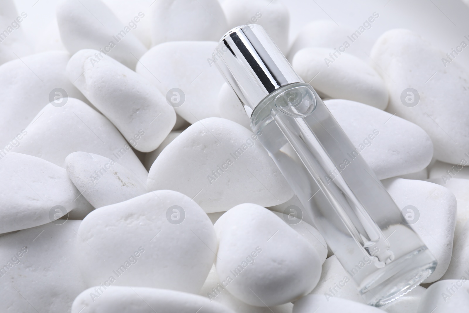 Photo of Bottle of serum on white pebble stones, closeup