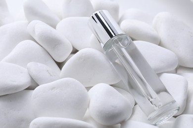 Bottle of serum on white pebble stones, closeup