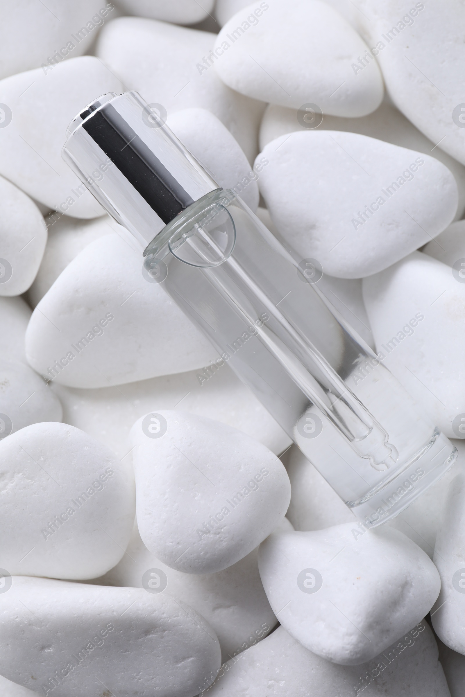 Photo of Bottle of serum on white pebble stones, top view