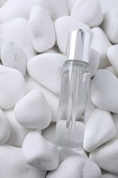 Bottle of serum on white pebble stones, top view