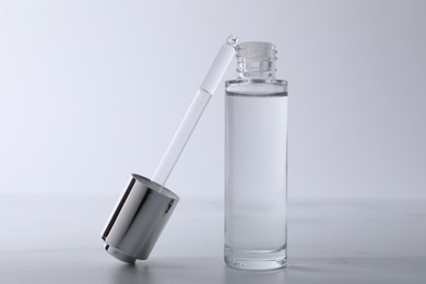 Bottle and pipette of serum on light grey table, closeup