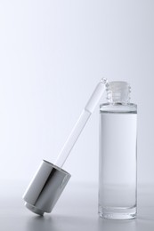 Bottle and pipette of serum on light grey table, closeup