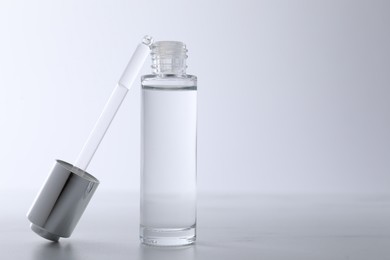 Photo of Bottle and pipette of serum on light grey table, closeup. Space for text