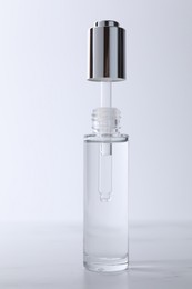 Photo of Bottle and pipette of serum on light grey table, closeup