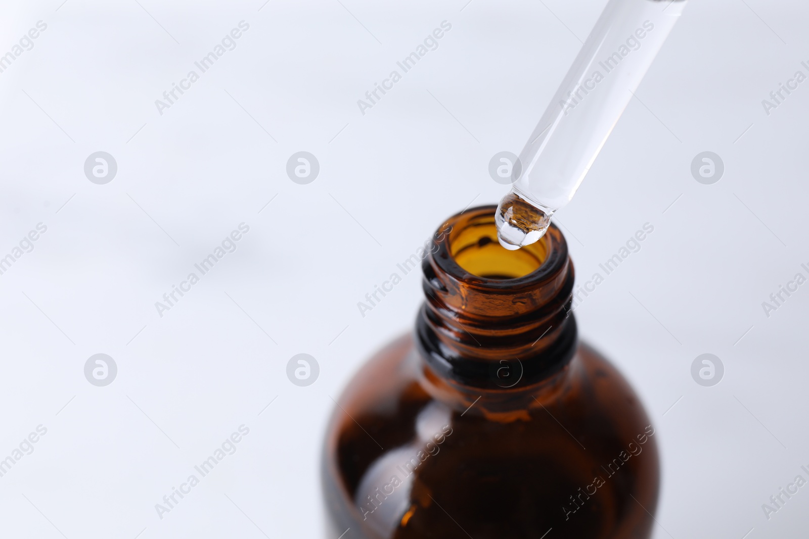 Photo of Dripping serum from pipette into bottle on light background, closeup. Space for text