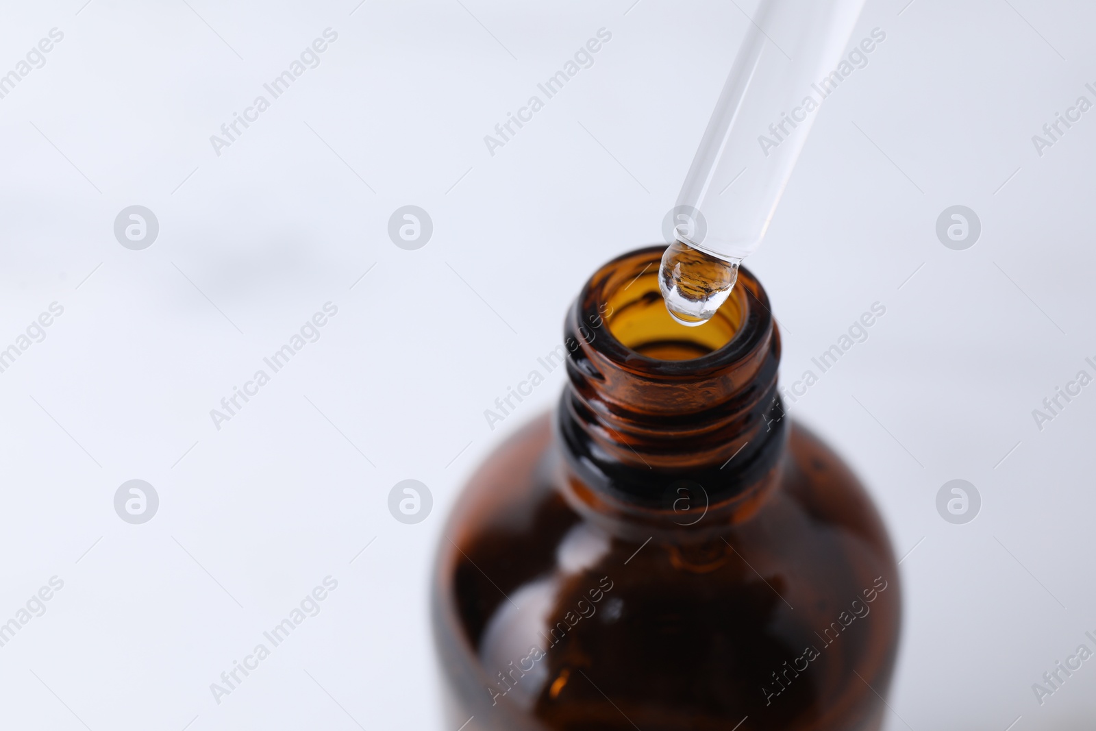 Photo of Dripping serum from pipette into bottle on light background, closeup. Space for text