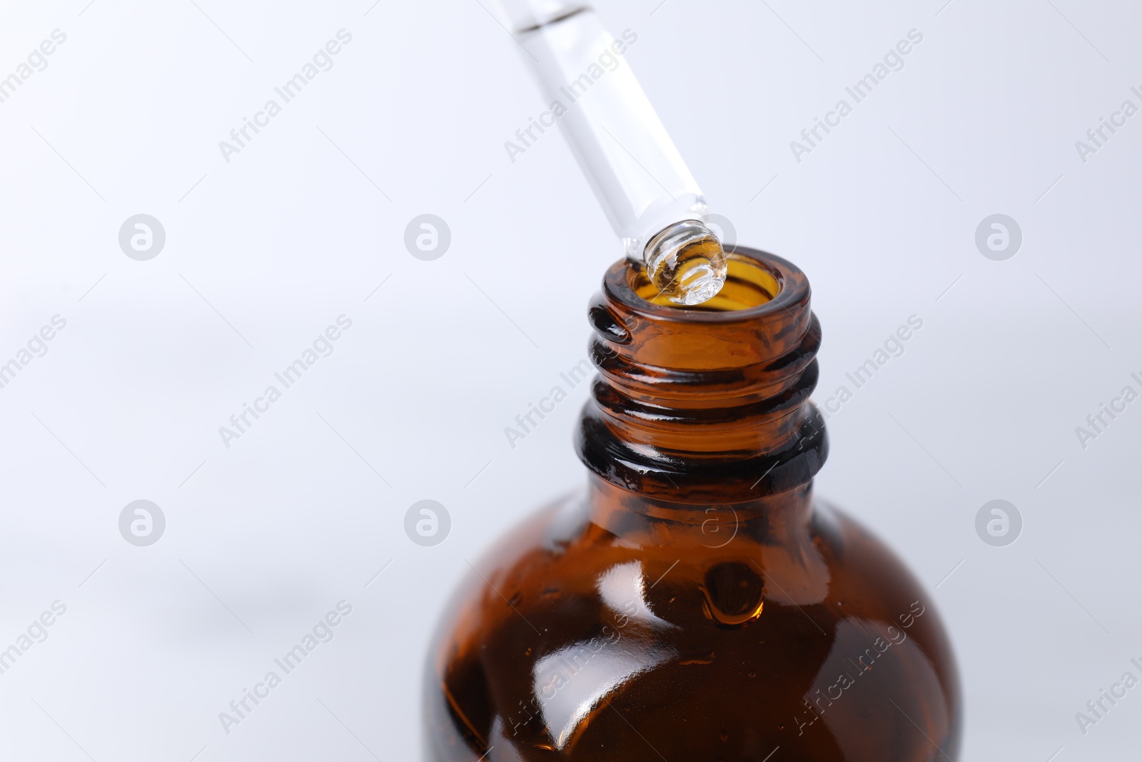 Photo of Dripping serum from pipette into bottle on light background, closeup. Space for text