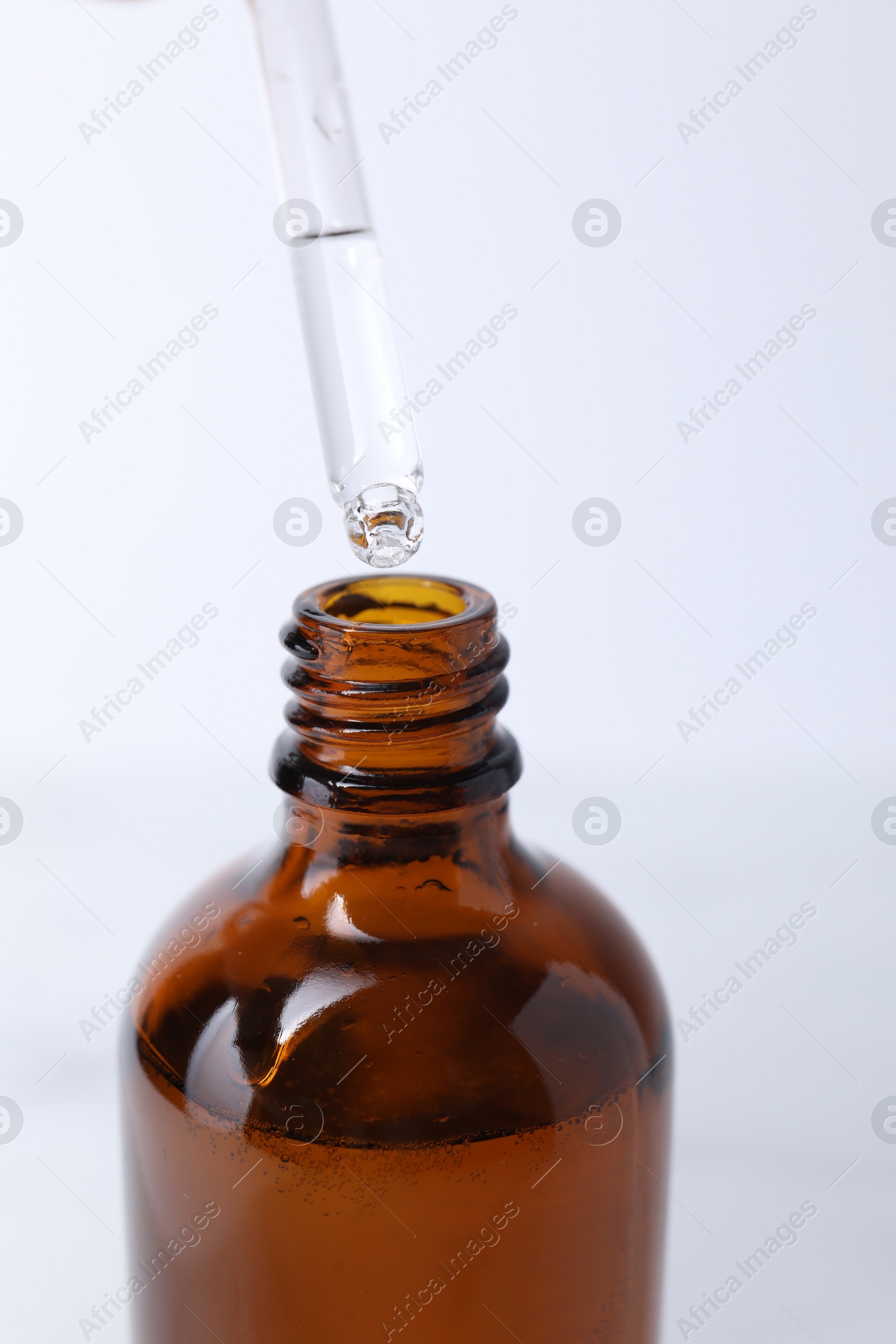 Photo of Dripping serum from pipette into bottle on light background, closeup