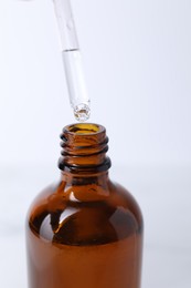 Photo of Dripping serum from pipette into bottle on light background, closeup