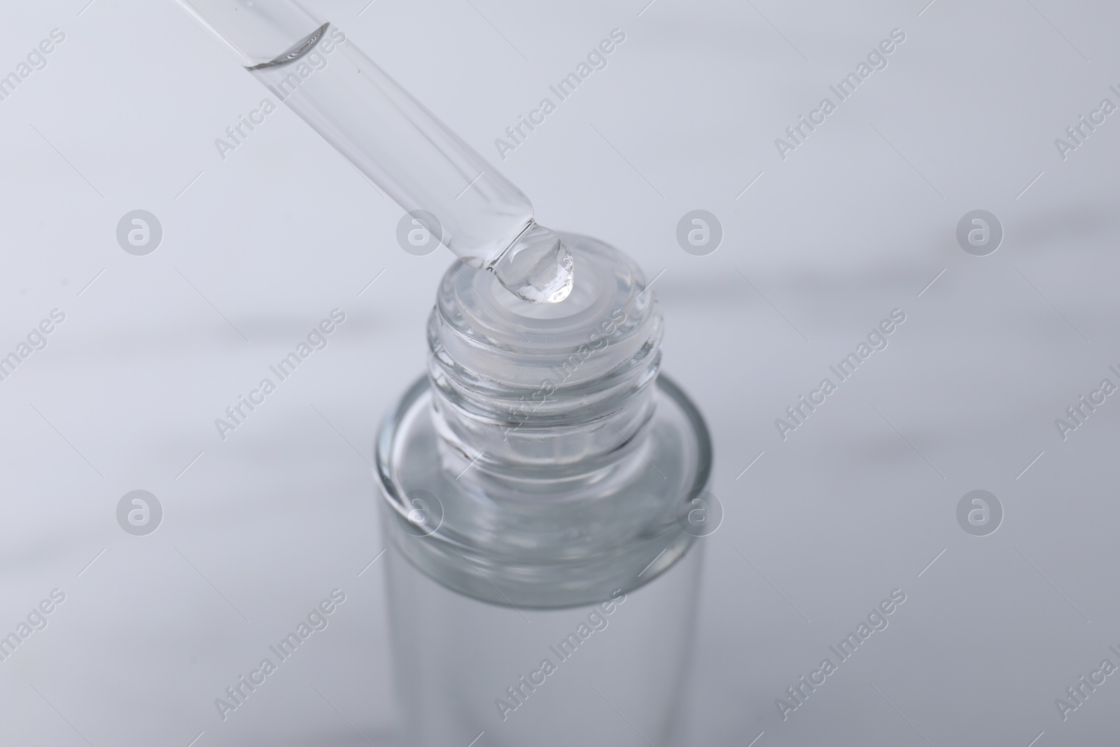 Photo of Dripping serum from pipette into bottle on light grey background, closeup