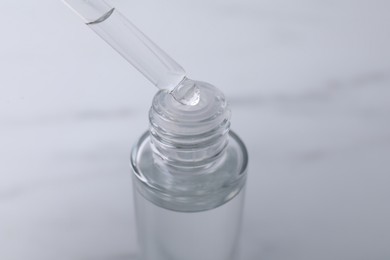 Dripping serum from pipette into bottle on light grey background, closeup