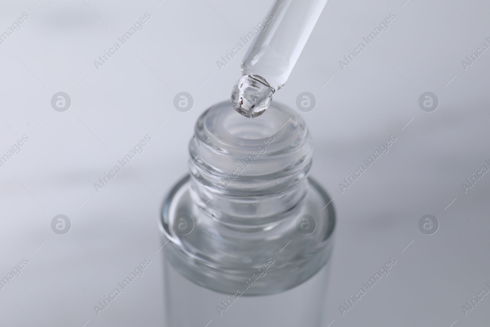 Photo of Dripping serum from pipette into bottle on light grey background, closeup