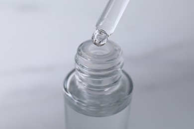 Photo of Dripping serum from pipette into bottle on light grey background, closeup