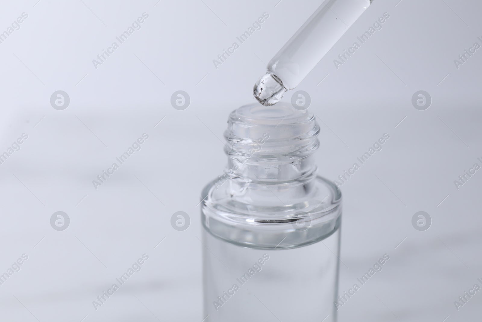 Photo of Dripping serum from pipette into bottle on light grey background, closeup. Space for text