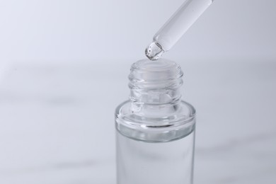 Dripping serum from pipette into bottle on light grey background, closeup. Space for text