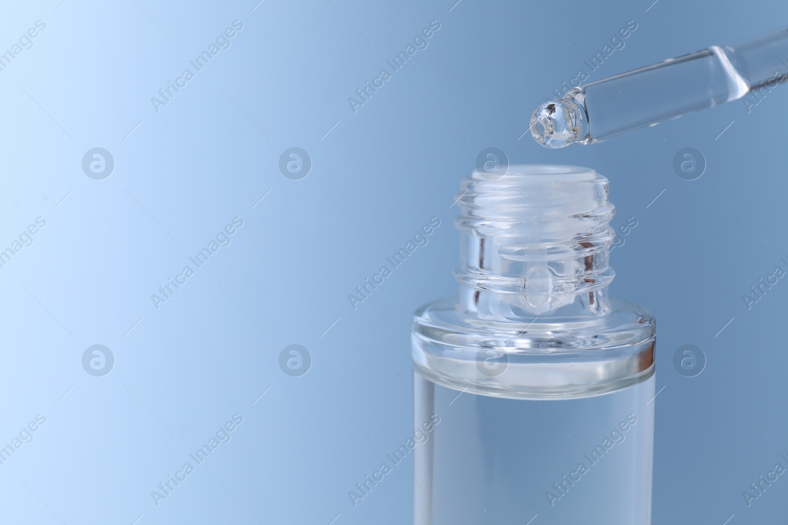 Photo of Dripping serum from pipette into bottle on light blue background, closeup. Space for text