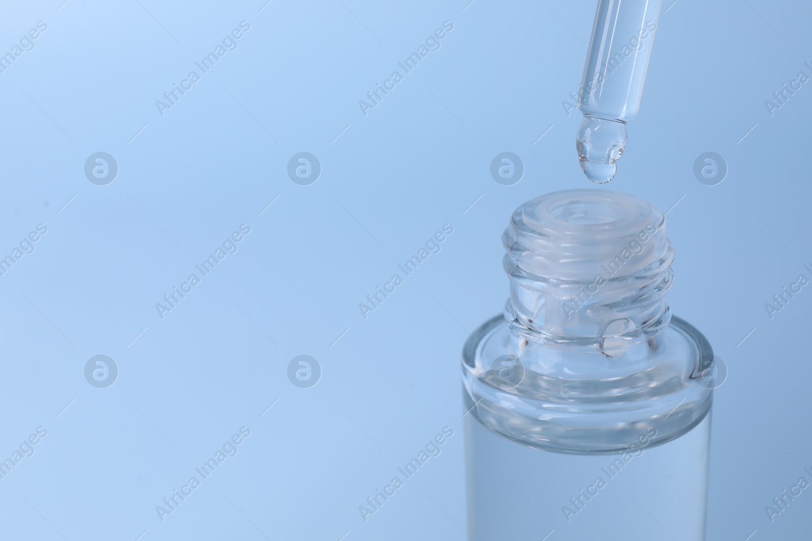 Photo of Dripping serum from pipette into bottle on light blue background, closeup. Space for text