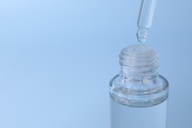 Dripping serum from pipette into bottle on light blue background, closeup. Space for text