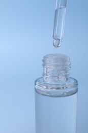 Dripping serum from pipette into bottle on light blue background, closeup