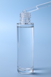 Photo of Dripping serum from pipette into bottle on light blue background, closeup