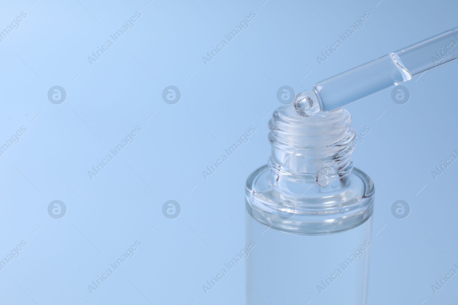 Photo of Dripping serum from pipette into bottle on light blue background, closeup. Space for text