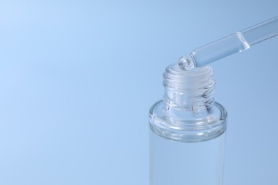 Dripping serum from pipette into bottle on light blue background, closeup. Space for text