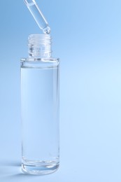 Photo of Dripping serum from pipette into bottle on light blue background, closeup. Space for text