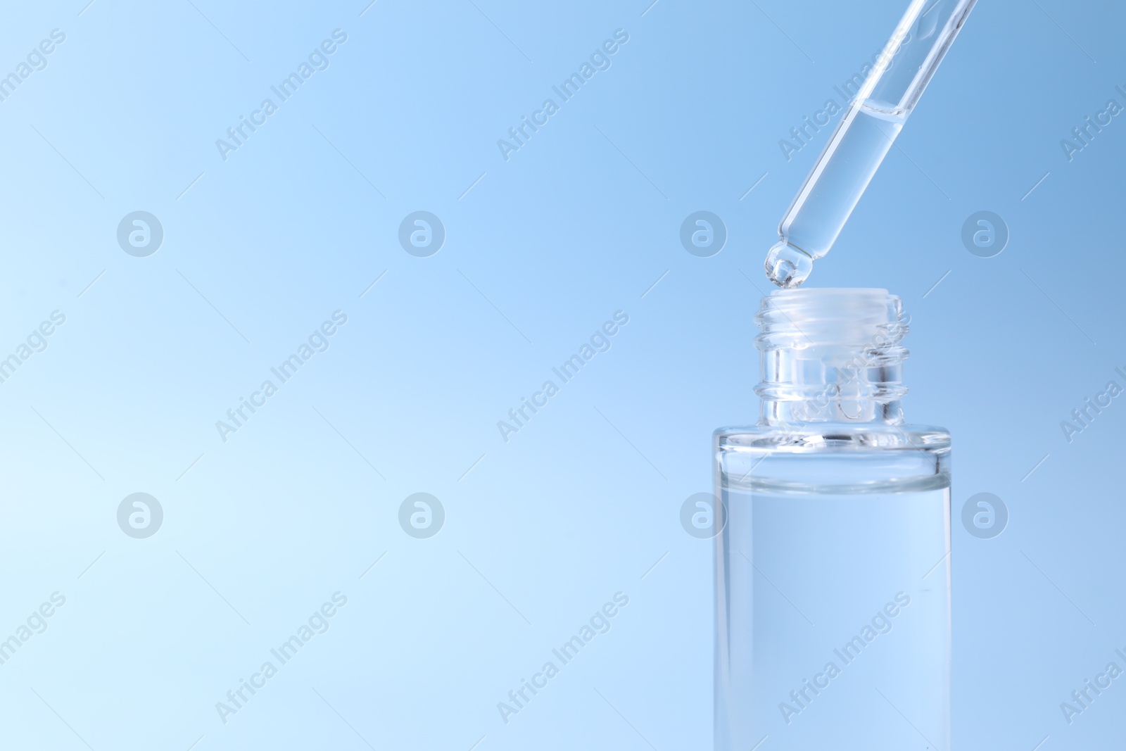 Photo of Dripping serum from pipette into bottle on light blue background, closeup. Space for text