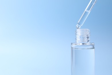 Dripping serum from pipette into bottle on light blue background, closeup. Space for text