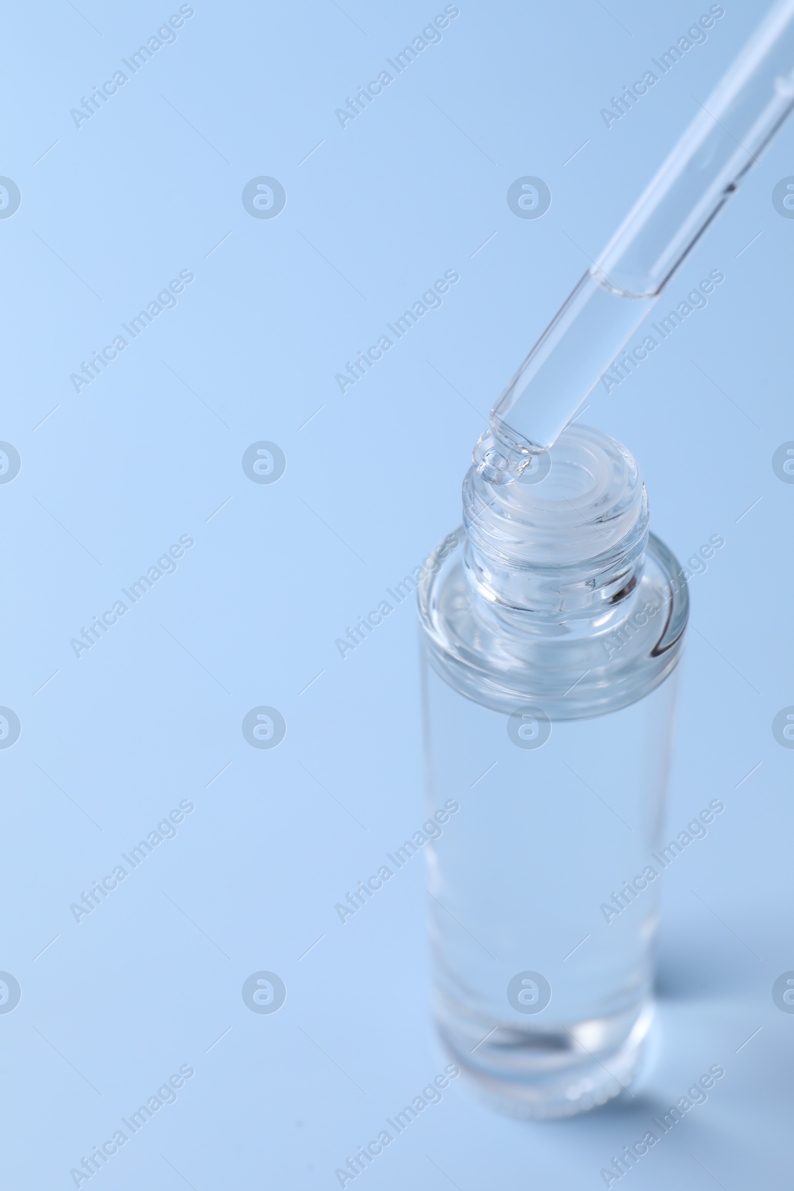 Photo of Dripping serum from pipette into bottle on light blue background, closeup. Space for text