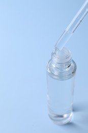 Photo of Dripping serum from pipette into bottle on light blue background, closeup. Space for text