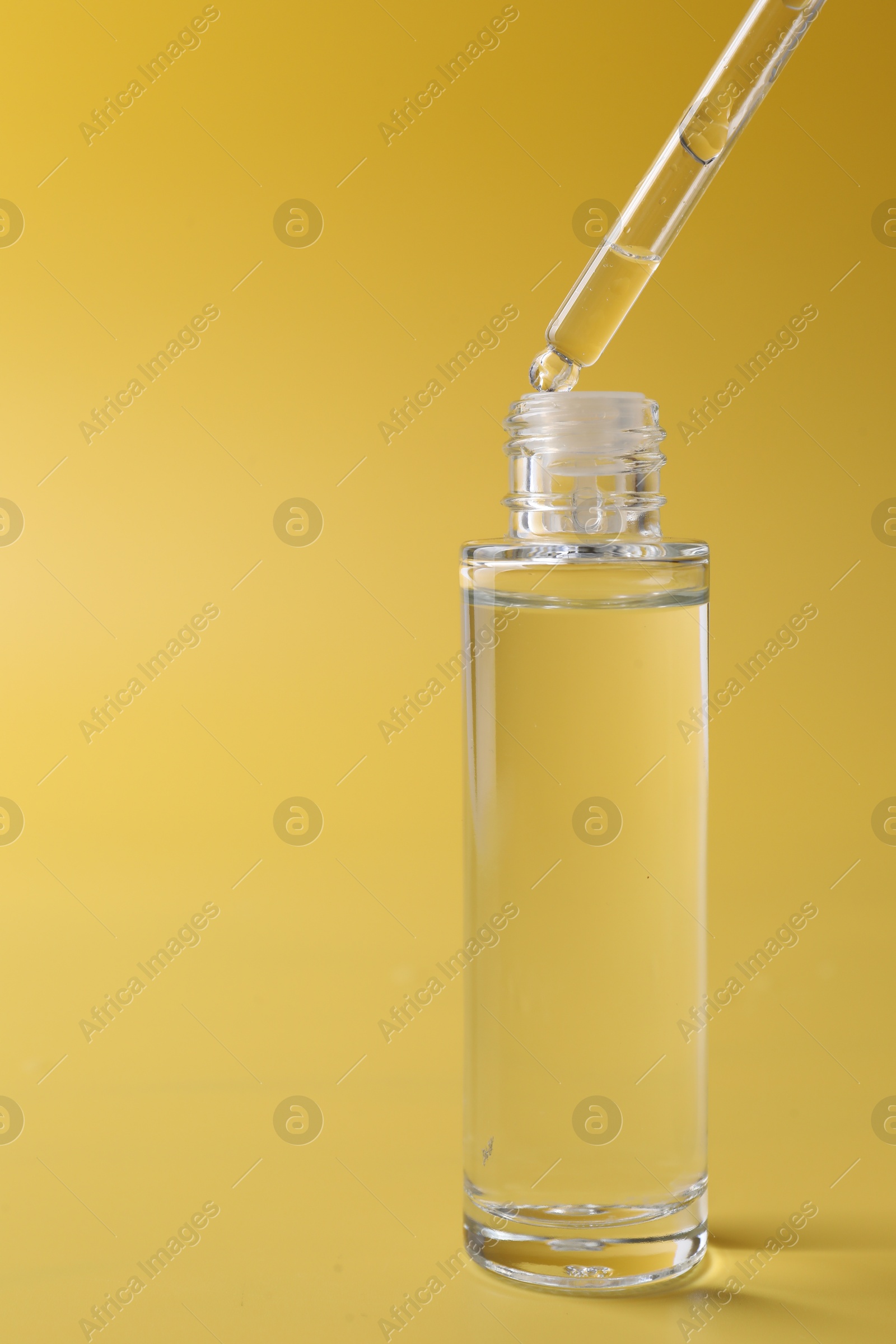 Photo of Dripping serum from pipette into bottle on yellow background, closeup. Space for text