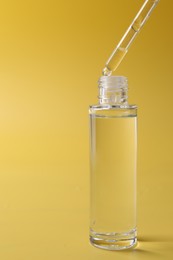 Dripping serum from pipette into bottle on yellow background, closeup. Space for text