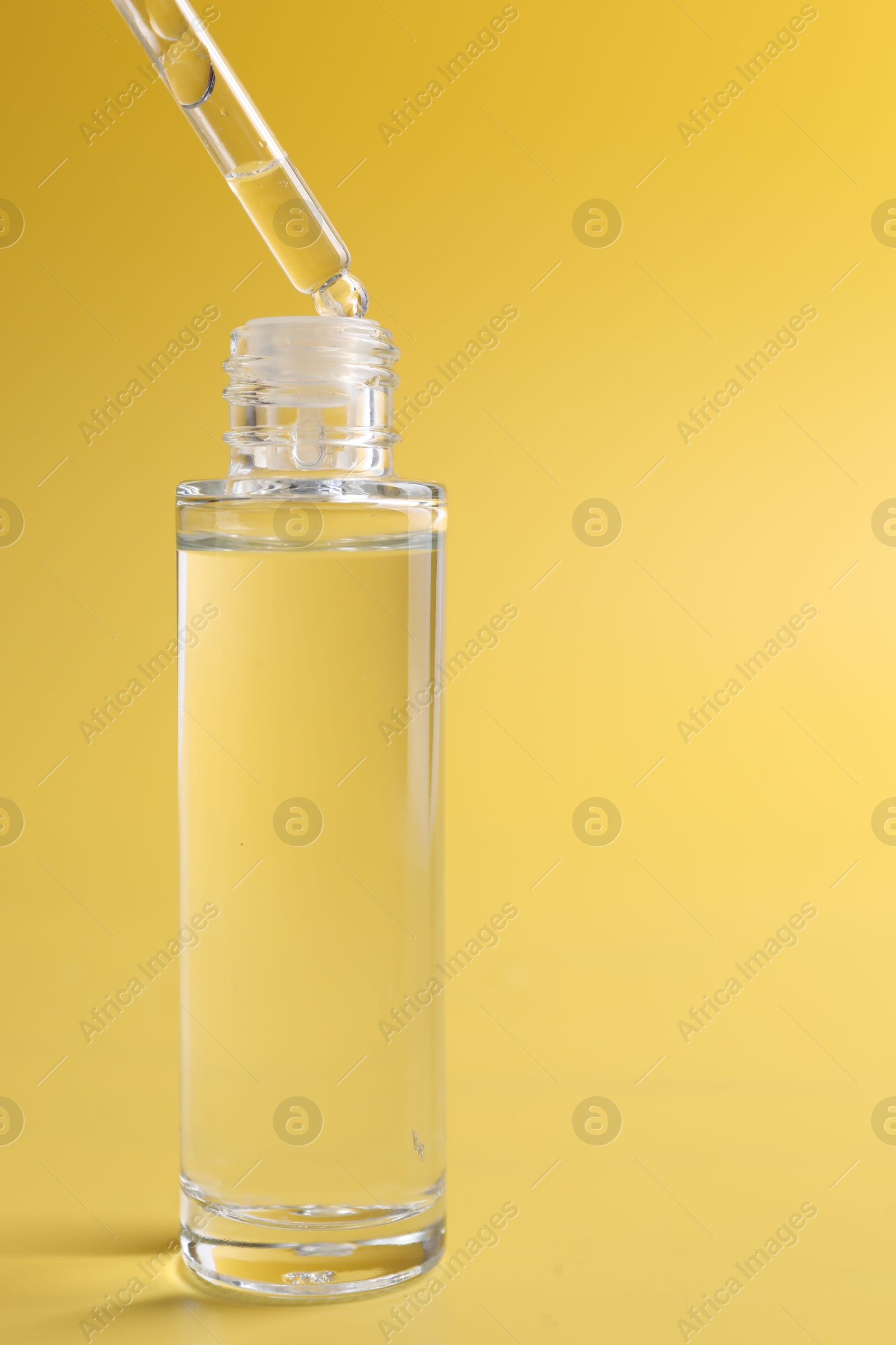 Photo of Dripping serum from pipette into bottle on yellow background, closeup. Space for text