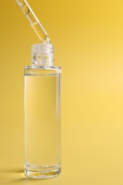 Photo of Dripping serum from pipette into bottle on yellow background, closeup. Space for text