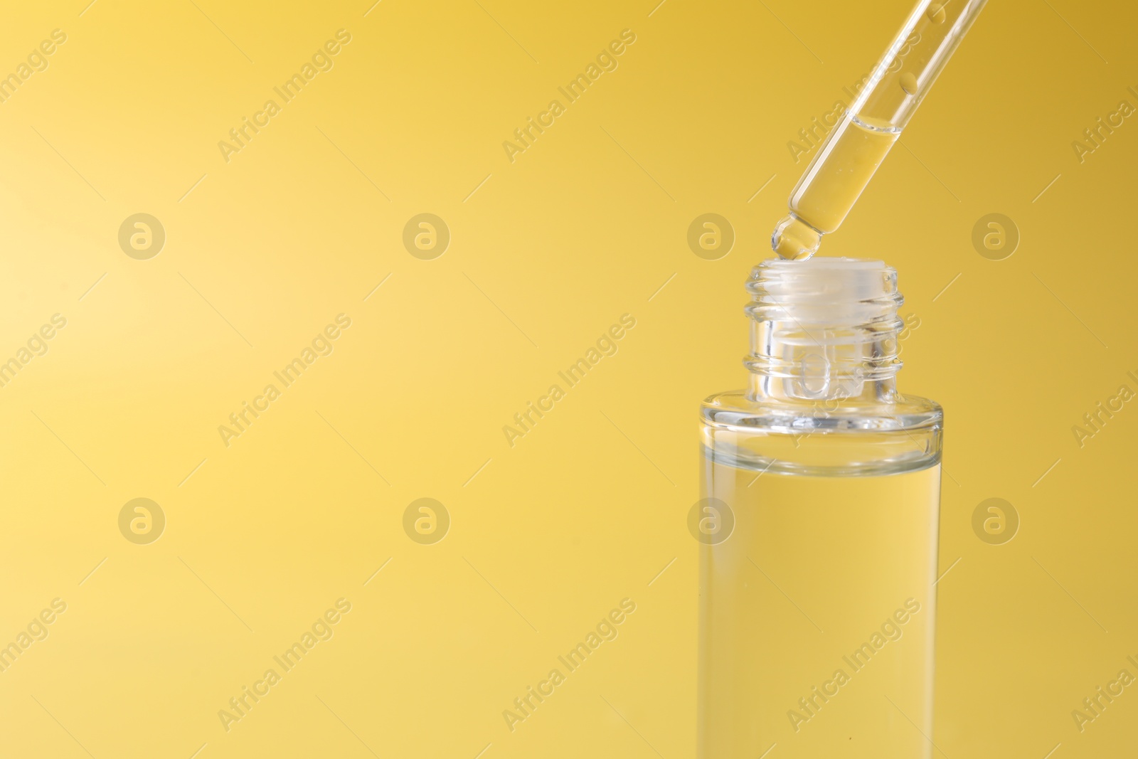 Photo of Dripping serum from pipette into bottle on yellow background, closeup. Space for text