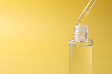 Dripping serum from pipette into bottle on yellow background, closeup. Space for text